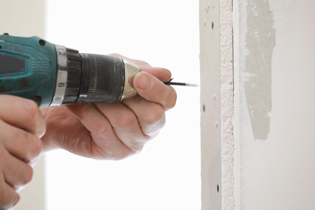 Main d'un homme qui fait visser du placo sur le mur