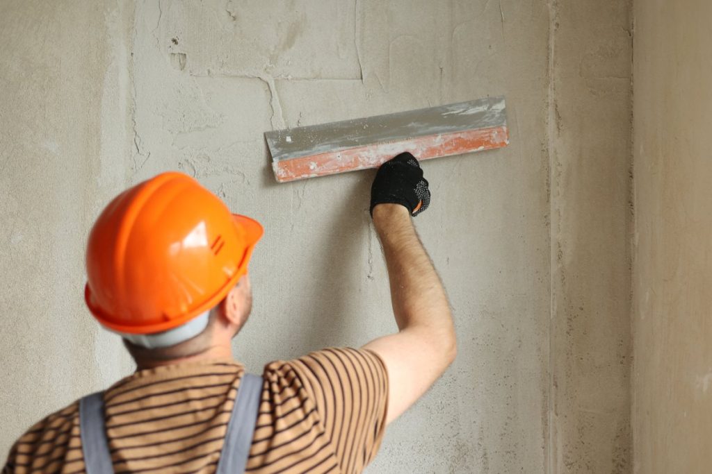 Un ouvrier portant un casque et enduisant le mur au chaux plâtre